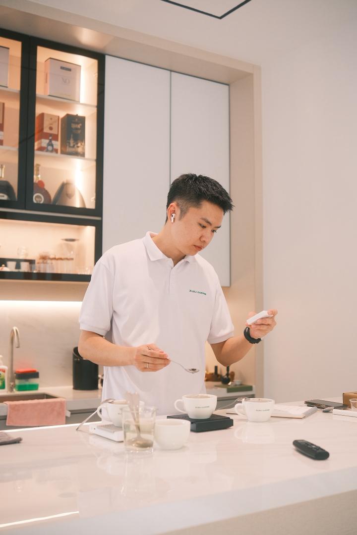 A ZuZu Coffee team member holding a cup in a warm studio setting.